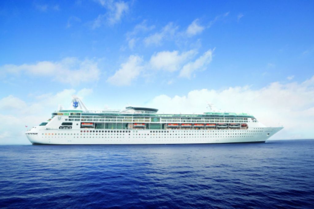 The 'Grandeur of the Seas' cruise ship travels in the open sea, its white structure contrasting with the deep blue waters, under a sky scattered with white clouds, embodying the essence of ocean travel.