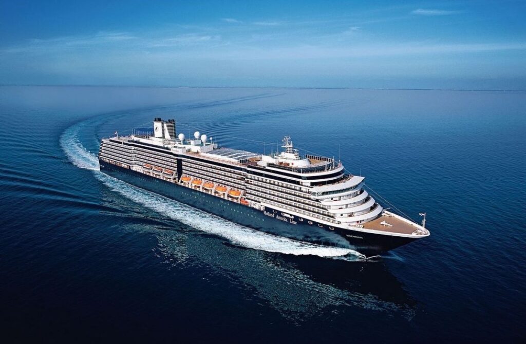 The MS Noordam cruise ship of Holland America Line majestically sails the calm blue ocean, leaving a trail of white foam as it cuts through the water.