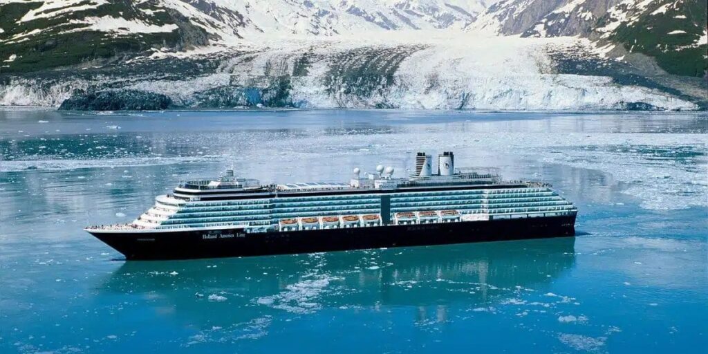 A photo of the MS Oosterdam, Holland America cruise ship, sailing on the sea with snowy mountains in the background.