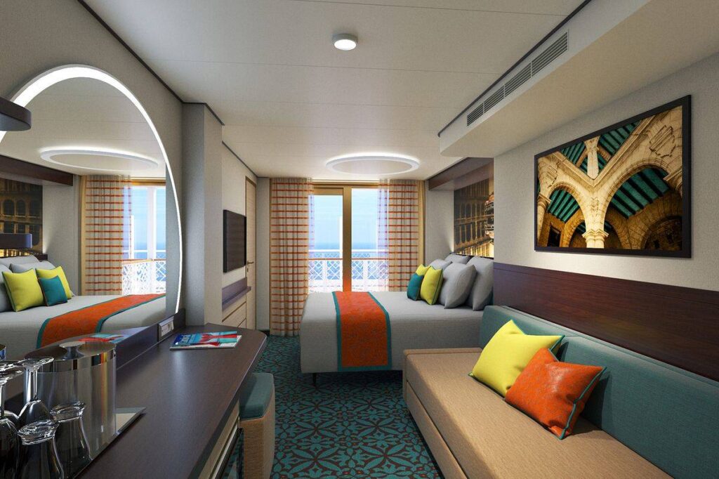 The Havana Cabana on Carnival Celebration features a spacious room with a refreshing coastal vibe, complete with a comfortable sofa adorned with colorful pillows, a large window offering ocean views, and vibrant artwork adding a touch of Cuban flair.