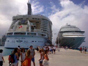 Multiple cruise ships docked at a port with passengers boarding and walking on the pier