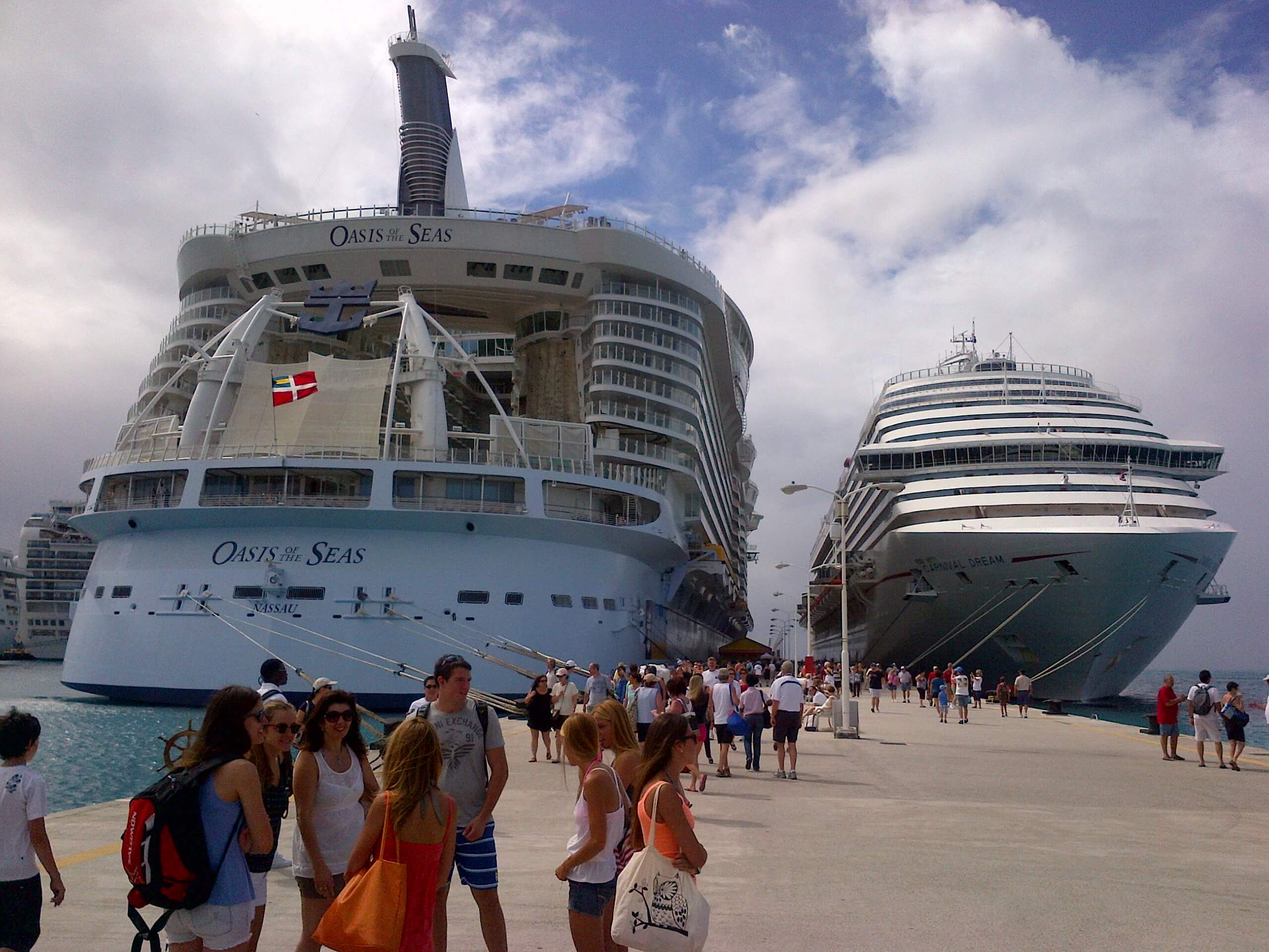 Multiple cruise ships docked at a port with passengers boarding and walking on the pier