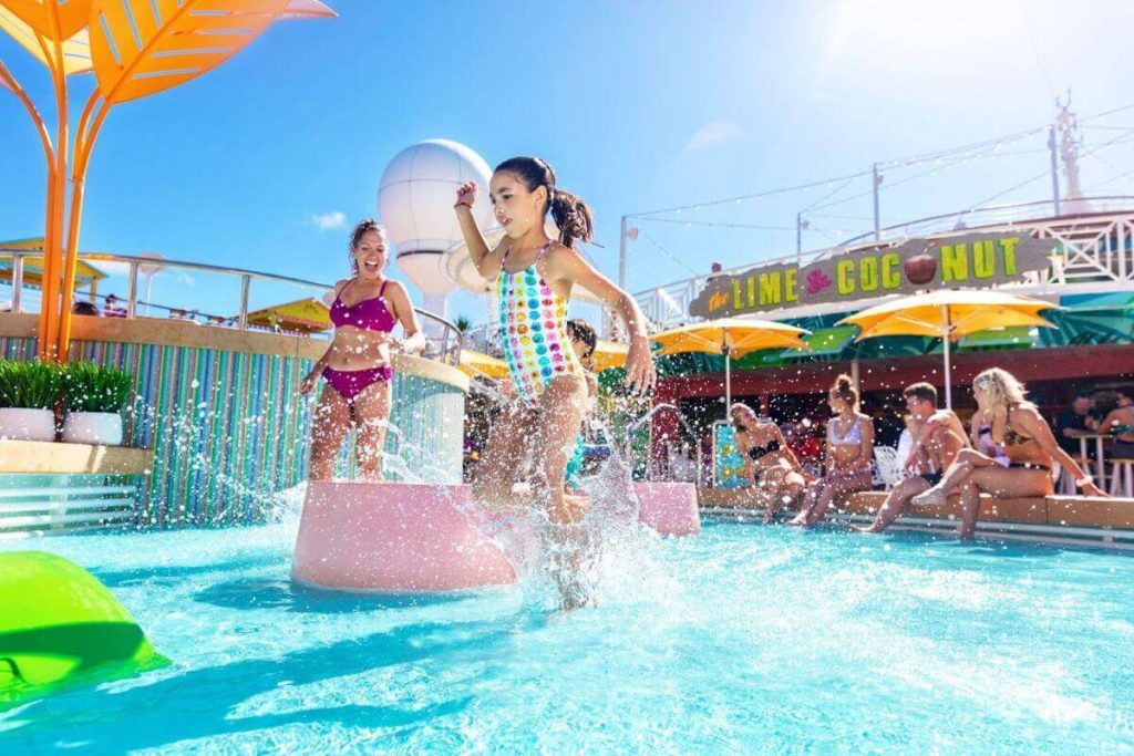 Children playing joyfully in the splash zone at the vibrant and sunny water park on Royal Caribbean's Icon of the Seas, with lively surroundings and the 'Lime & Coconut' bar in the background.