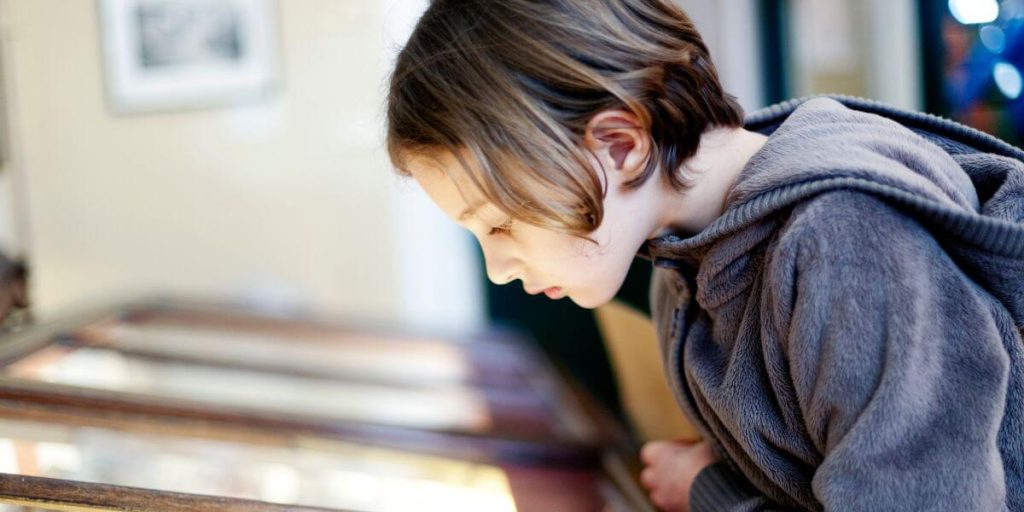 A young child with short hair, engrossed in viewing an exhibit at the Belize City Museum, the natural lighting accentuating their contemplative expression.