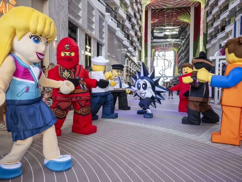 Large costumed LEGO characters interact with guests inside a bright, open atrium on an MSC cruise ship.