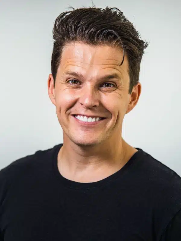 Lee Mason, Carnival cruise director, smiling in a studio-style portrait against a light background.