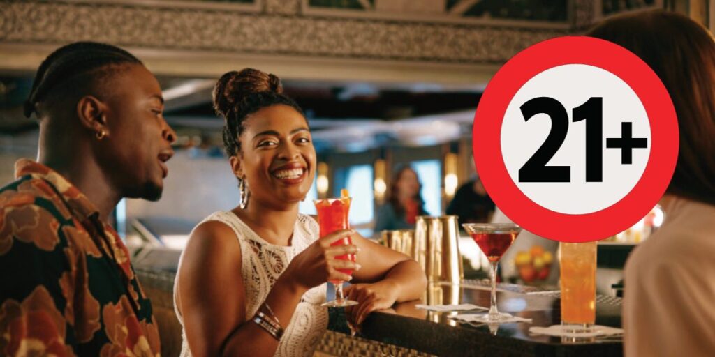 A joyful couple at a bar with a woman holding a cocktail, laughing with her companion, under a sign with '21+' indicating an age restriction for alcohol consumption.