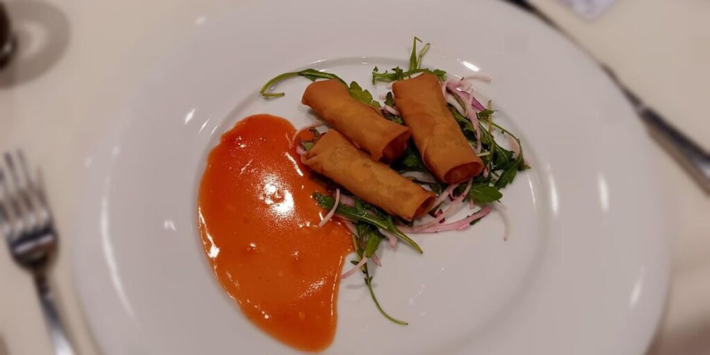 A delicious looking lumpia dish served on a clean white plate with a sweet and spicy sauce. 