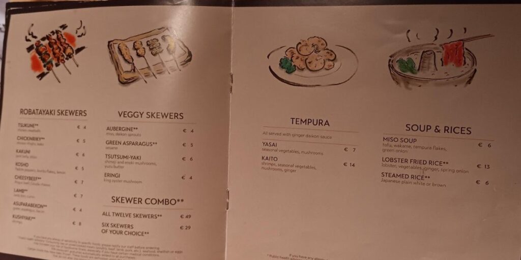 Menu selections from a restaurant featuring a variety of Japanese dishes. The 'Robatayaki Skewers' section offers options like 'Chicken Yakitori' and 'Cheese Beef,' while 'Veggy Skewers' include 'Aubergine' and 'Green Asparagus.' 'Tempura' dishes are served with ginger daikon sauce, and 'Soup & Rices' feature 'Miso Soup' and 'Lobster Fried Rice.' Prices range from €4 to €14, and a 'Skewer Combo' is available.