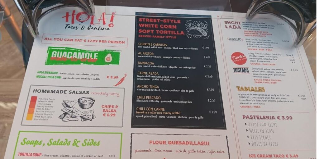 Menu from 'Hola! Tacos & Cantina' featuring a variety of Mexican dishes. Highlights include 'All You Can Eat' for £17.99 per person, 'Guacamole made to order,' homemade salsas like 'Habanera Fuego' and 'Salsa Verde,' along with street-style 'White Corn Soft Tortilla' options such as 'Chipotle Carnitas' and 'Barbacoa.' The menu also lists soups, salads, sides, and desserts like 'Arroz con Leche' and 'Mexican Flan.