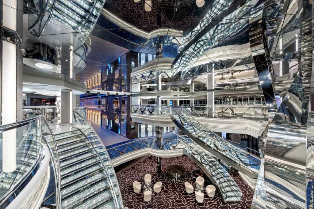 The opulent Swarovski crystal staircases inside MSC Euribia sparkle brilliantly, reflecting the intricate patterns of light across multiple levels of the ship's elegant interior, surrounded by sleek modern design elements and a tranquil lounge area below.