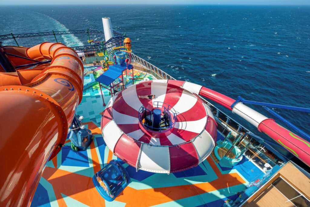 Overhead view of the colorful Aqua Park on MSC Euribia, showcasing a spiraling orange water slide, a spacious deck with geometric patterns, and the vast open sea stretching into the horizon under a clear blue sky.