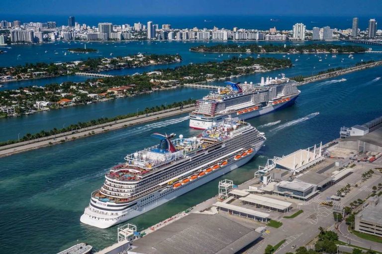 Aerial view of the Mardi Gras cruise ship in Miami, flanked by the vibrant blue waters of the bay with the city's lush residential areas in the backdrop.