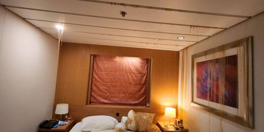 Interior of a stateroom on the Marella Explorer 2 cruise ship showing severe water damage, with brown stains streaking down the ceiling and walls, visible leaks, and a soaked bed and artwork. The image highlights ongoing maintenance issues reported aboard the Marella Explorer 2 cruise ship.