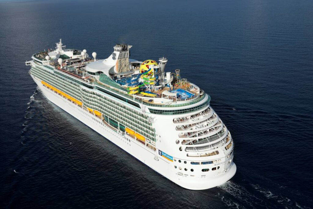 The Mariner of the Seas, a Royal Caribbean cruise ship, navigates the open sea, showcased from an aerial perspective. The ship's multiple colorful slides and outdoor activities hint at the adventure and entertainment aboard, contrasting with the vast and deep blue ocean below.