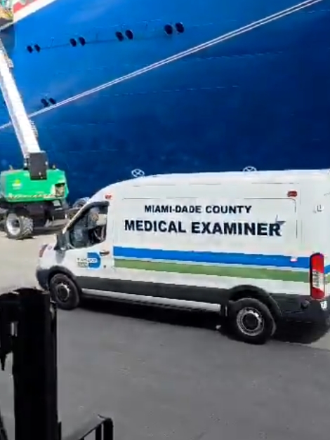 A Miami-Dade County Medical Examiner’s van parked beside the hull of a large cruise ship in PortMiami. The scene appears to be part of an official response following a reported passenger death onboard the vessel.