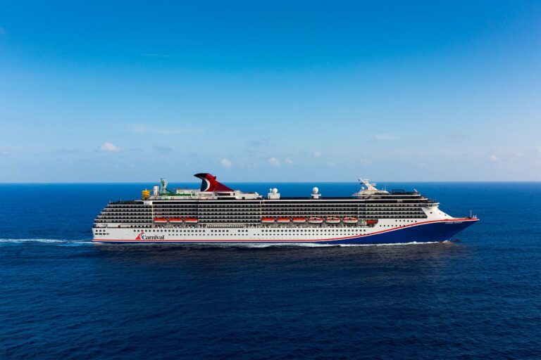 The Carnival Miracle cruise ship sails in the open ocean, its blue and white exterior gleaming under the clear blue sky, with the ship's red funnel adding a pop of color to the serene marine scene.