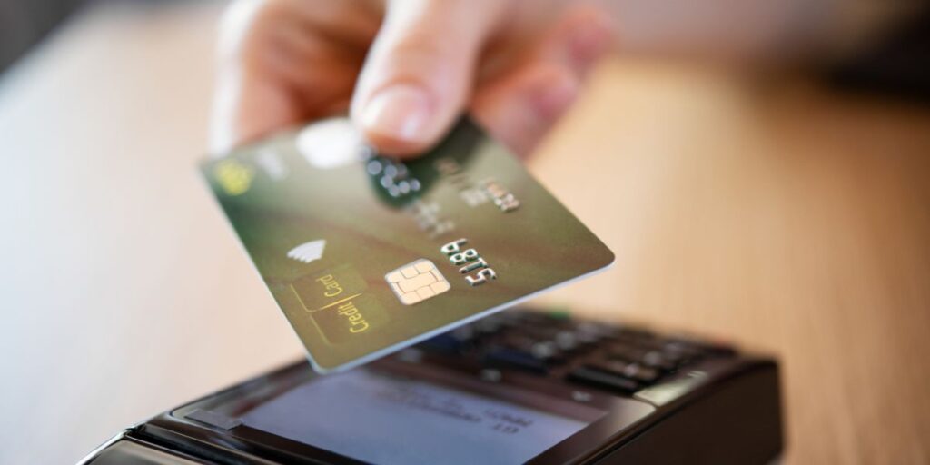 A close-up of a hand holding a green credit card over a payment terminal, ready to complete a transaction.