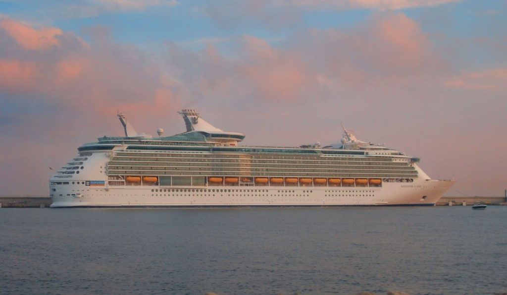 The Royal Caribbean Navigator of the Seas cruise ship captured at sunset, its silhouette highlighted against a sky of soft pastel hues, reflecting on the calm sea waters.
