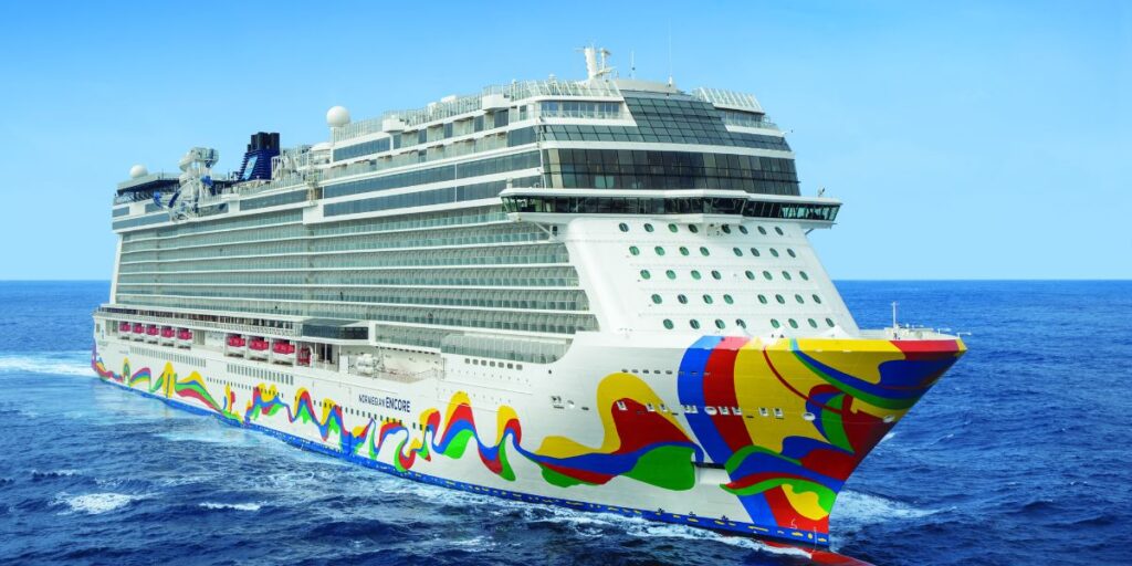 A colorful Norwegian Encore cruise ship sailing on the blue ocean, featuring a vibrant, multicolored hull artwork, under a clear sky.