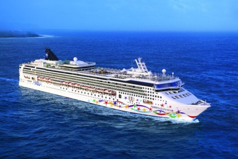 This image captures the Norwegian Star cruise ship sailing through deep blue ocean waters with a faint shoreline visible in the distance. The ship’s hull features colorful star-themed artwork, giving it a playful and festive appearance. Its sleek design and the surrounding serene seascape create an inviting scene of luxury and relaxation.