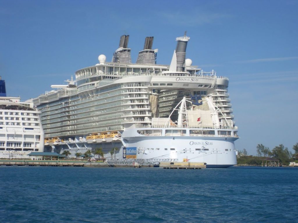 Royal Caribbean's Oasis of the Seas cruise ship moored in the Bahamas, its grand architecture dwarfing nearby structures, with clear blue skies and turquoise waters enhancing the tropical ambiance.