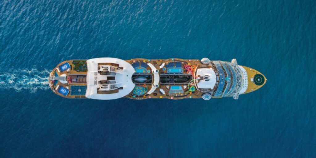 This aerial image provides a top-down view of the Oasis of the Seas cruise ship, showcasing its impressive layout and amenities. The ship features multiple pools, water slides, sports courts, and sun deck areas, highlighting its expansive and activity-filled design. The vibrant blue of the surrounding ocean contrasts beautifully with the colorful and dynamic ship, emphasizing its grandeur and entertainment-focused offerings.