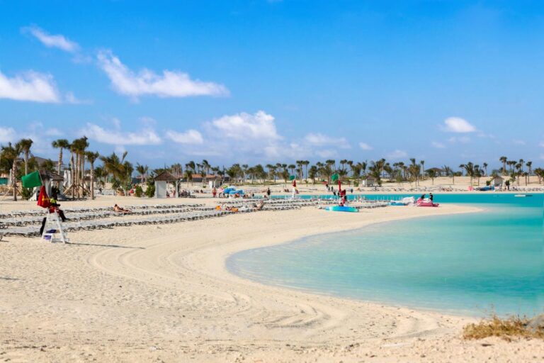 Scenic view of Ocean Cay MSC Marine Reserve with visitors enjoying the pristine sandy beach, crystal-clear turquoise waters, and abundant palm trees under a sunny sky with soft clouds.