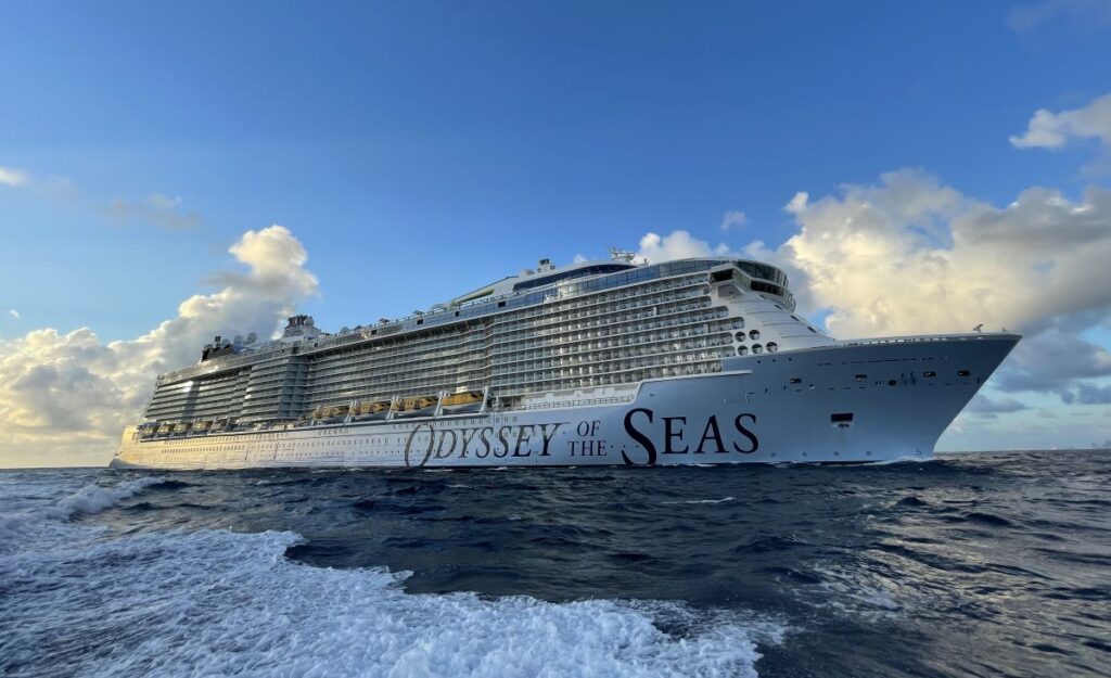 The Odyssey of the Seas, Royal Caribbean's quantum ultra-class cruise ship, makes its way through the deep blue ocean, under a sky with dramatic clouds at dusk. The ship's side is adorned with its name, marking its impressive presence on the high seas.