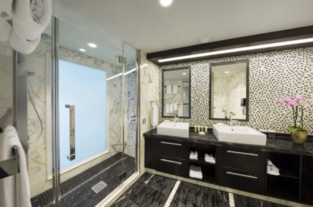 Elegant bathroom in the Owner's Loft Suite on Royal Caribbean's Anthem of the Seas, featuring dual sinks, marble countertops, and a spacious glass-enclosed shower with a view of the ocean.