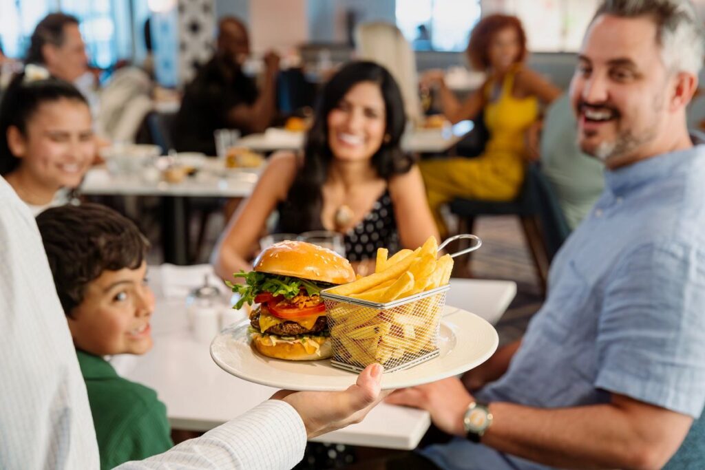 Server bringing a burger and fries to a smiling family dining together on a Princess Cruises ship.