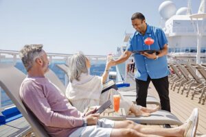 Princess cruise ship server brings drinks to two passengers relaxing on sun loungers on an outdoor deck.