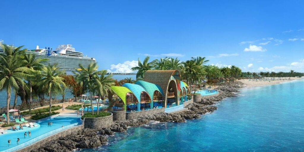 A vibrant tropical scene at Royal Caribbean's Party Cove at the Royal Beach Club in Nassau, featuring a colorful waterfront pavilion with curved roofs, surrounded by palm trees, a lazy river-style pool, and oceanfront rocky edges. A large cruise ship is docked nearby under a clear blue sky.