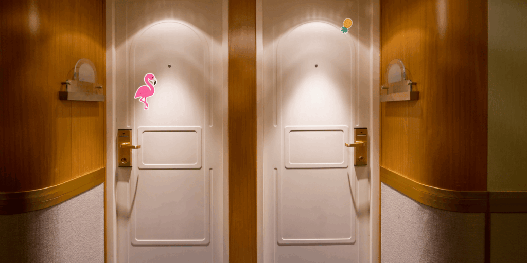 Two adjacent cruise ship cabin doors are shown in a hallway. The left door has a pink flamingo magnet decoration, while the right door has a pineapple magnet decoration. The corridor has wood paneling, wall sconces, and gold-colored door handles.