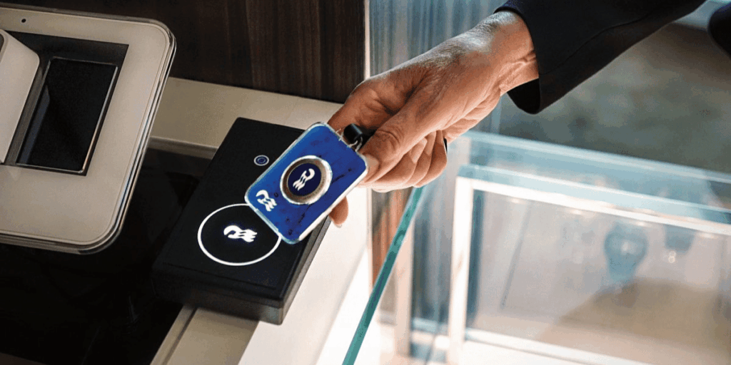 Close-up of a person tapping a Princess Cruises Medallion encased in a keychain holder on a contactless payment terminal. The glowing logo on the reader emphasizes the Medallion’s functionality for secure and convenient onboard purchases.