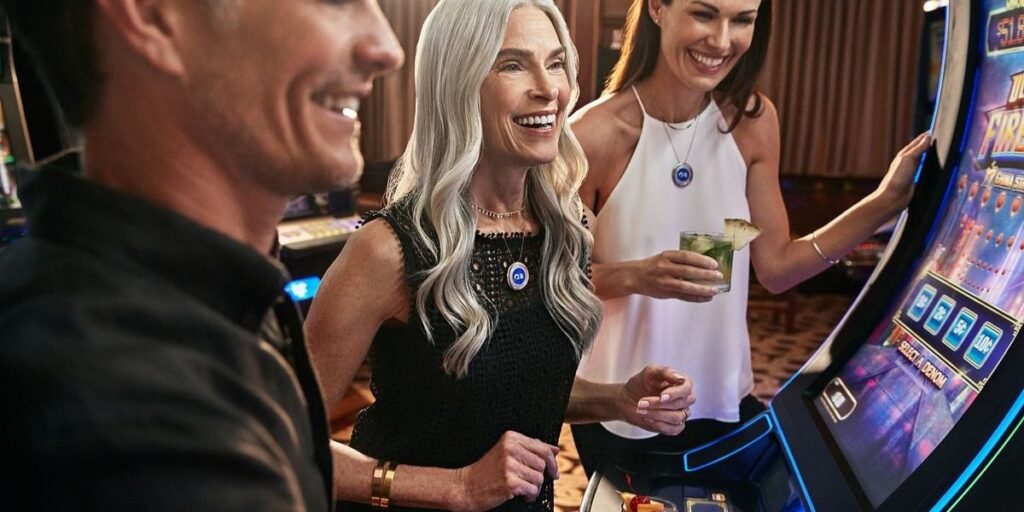 Three adults enjoy playing slot machines in a cruise ship casino, smiling and relaxed. Two women wear Princess Cruises Medallions as necklaces, showcasing how the device integrates with onboard activities and transactions.
