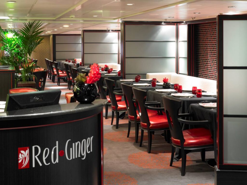 This image depicts Red Ginger, a sophisticated dining venue aboard an Oceania cruise ship. The restaurant is elegantly decorated with a modern Asian-inspired design, featuring black and red accents, sleek furnishings, and decorative touches like bold floral centerpieces. The intimate atmosphere and stylish decor create a luxurious setting for guests to enjoy fine dining.