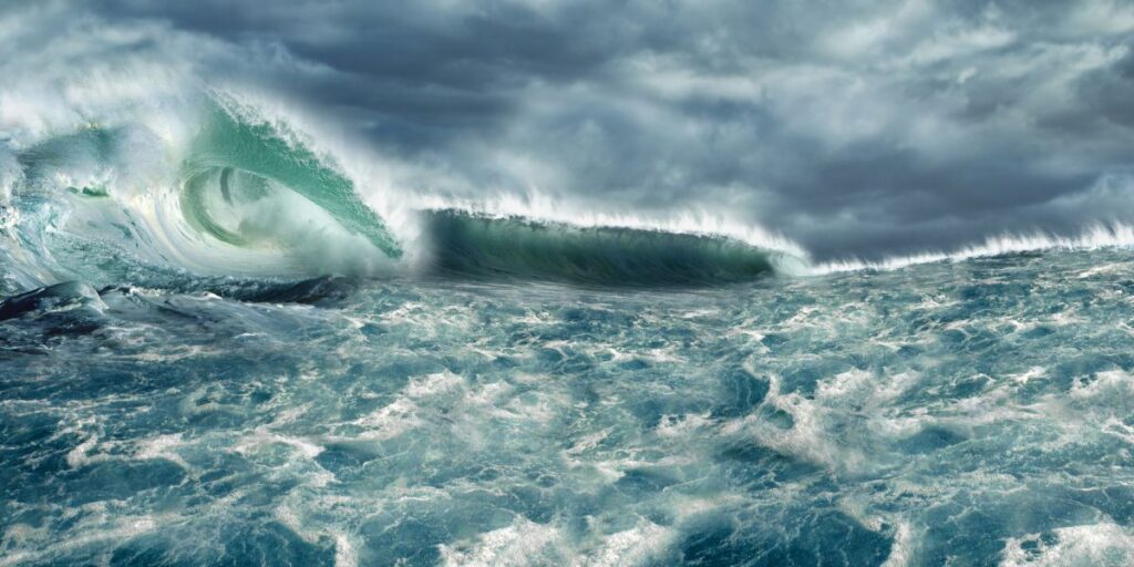 A towering wave crests dramatically under a tumultuous sky, illustrating the raw power of the ocean in a tempest. The churning turquoise waters foretell the intense conditions that can be encountered in the world's most challenging seas.