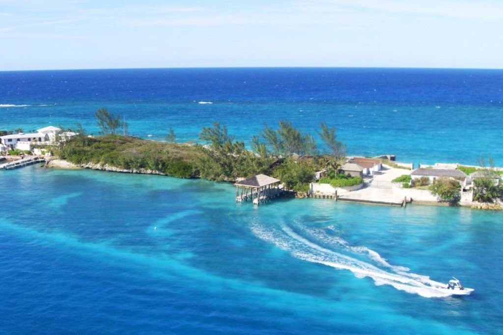 Panoramic ocean view from a Royal Caribbean balcony room overlooking the clear turquoise waters of the Bahamas with a speedboat cruising by a lush island.