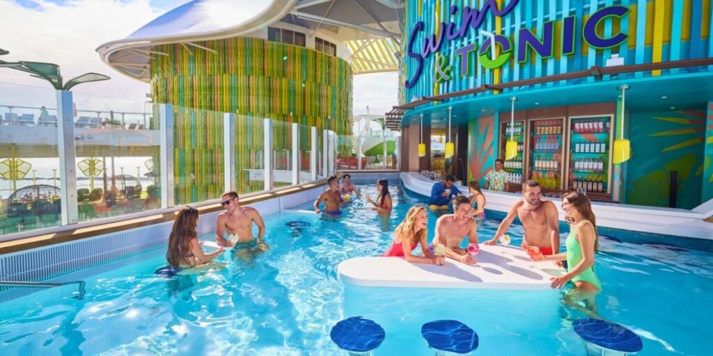 Guests enjoy colorful cocktails while lounging in a lively swim-up pool bar called “Swim & Tonic” aboard a cruise ship. Surrounded by vibrant decor, bar stools, and tropical vibes, the scene captures a fun, social atmosphere under the sun.