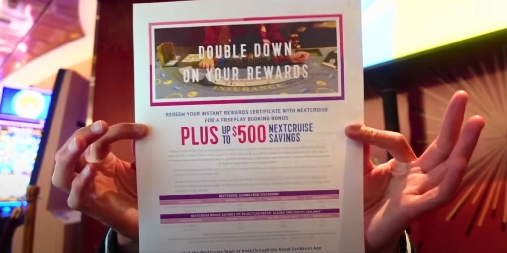A person holds up a Royal Caribbean casino flyer promoting "Double Down on Your Rewards," offering up to $500 in NextCruise savings and a freeplay booking bonus. The flyer includes a photo of a blackjack table and details about redeeming instant rewards with the cruise line's NextCruise program.