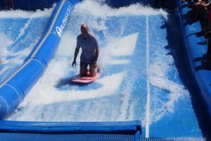 A guest enjoys surfing on the FlowRider surf simulator aboard the Oasis of the Seas cruise ship, showcasing an exciting on-board activity under clear blue skies.