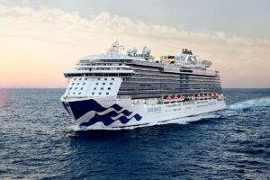 The Royal Princess cruise ship from Princess Cruises majestically sails the open sea, its white and blue livery glistening under the sun against a backdrop of calm blue waters and a soft sky.