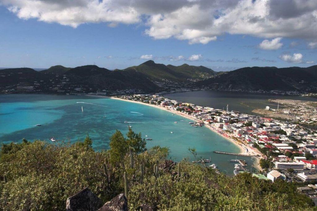Overlooking view of St. Maarten island, showcasing the stunning contrast between the serene turquoise Caribbean waters and the bustling coastal town nestled among rolling hills.