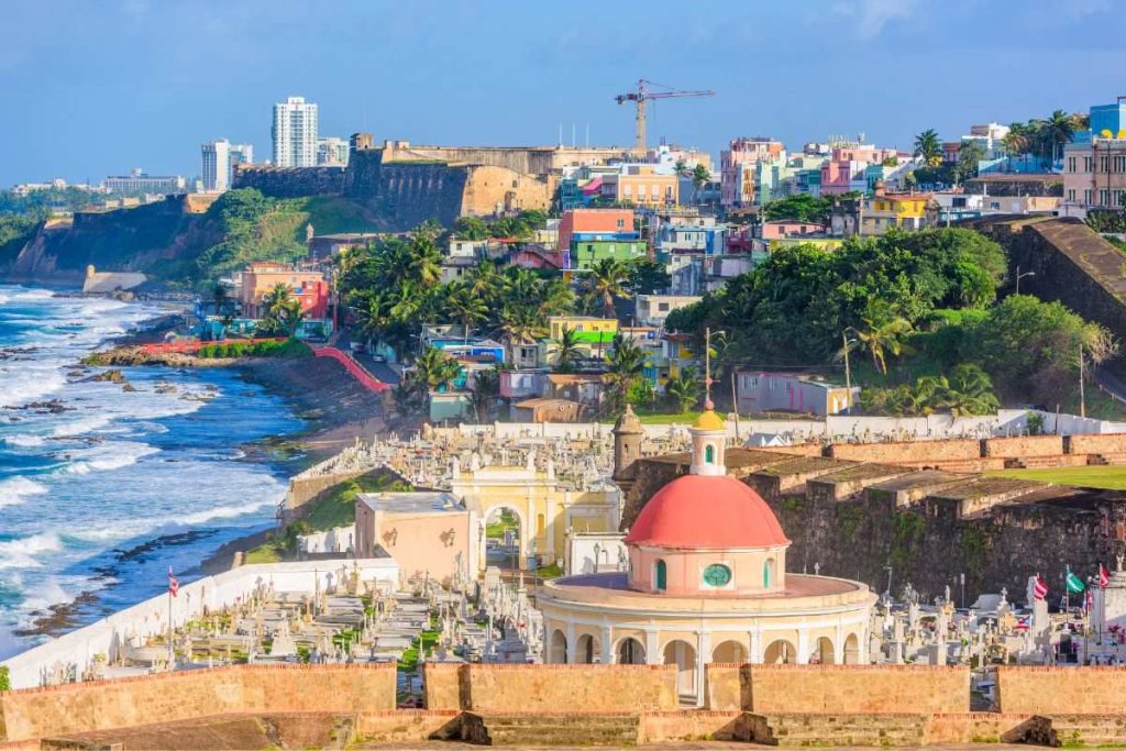 Historic San Juan, Puerto Rico, with its colorful buildings and colonial architecture overlooking the cemetery and the rough Atlantic waves, under a clear sky.