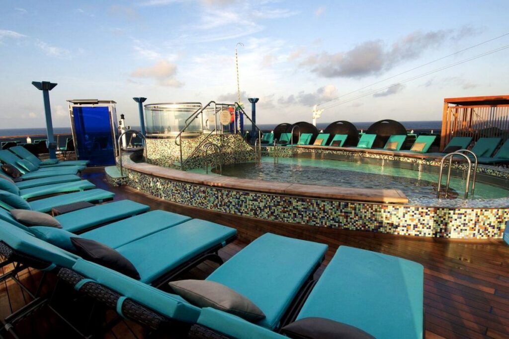 The Serenity Adult-Only Retreat on Carnival Miracle offers a peaceful escape with a soothing hot tub, plush teal loungers, and a panoramic ocean view in a calm and relaxing setting.