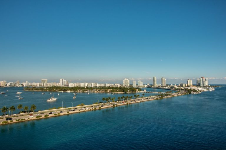 Panoramic view of PortMiami with clear blue skies, showcasing the bustling port area, surrounded by the tranquil waters of Biscayne Bay and Miami's distinctive skyline.