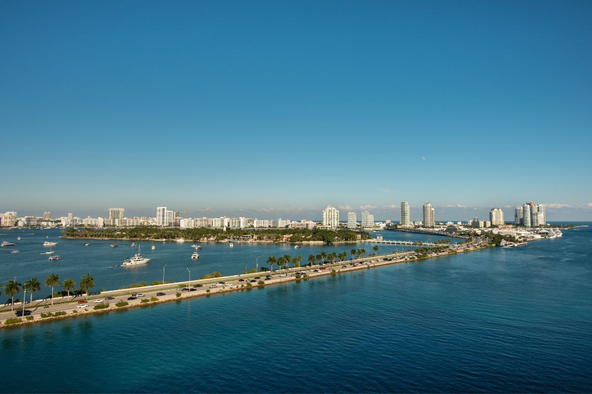 Panoramic view of PortMiami with clear blue skies, showcasing the bustling port area, surrounded by the tranquil waters of Biscayne Bay and Miami's distinctive skyline.