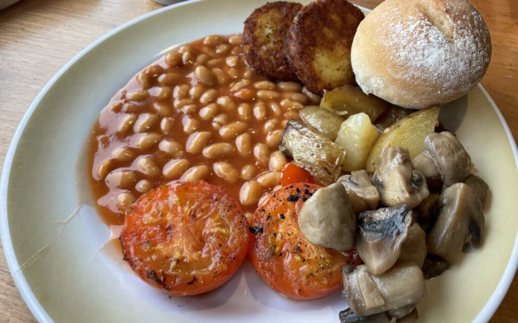 A hearty meal with baked beans, roasted vegetables, and a fresh dinner roll on a white plate.