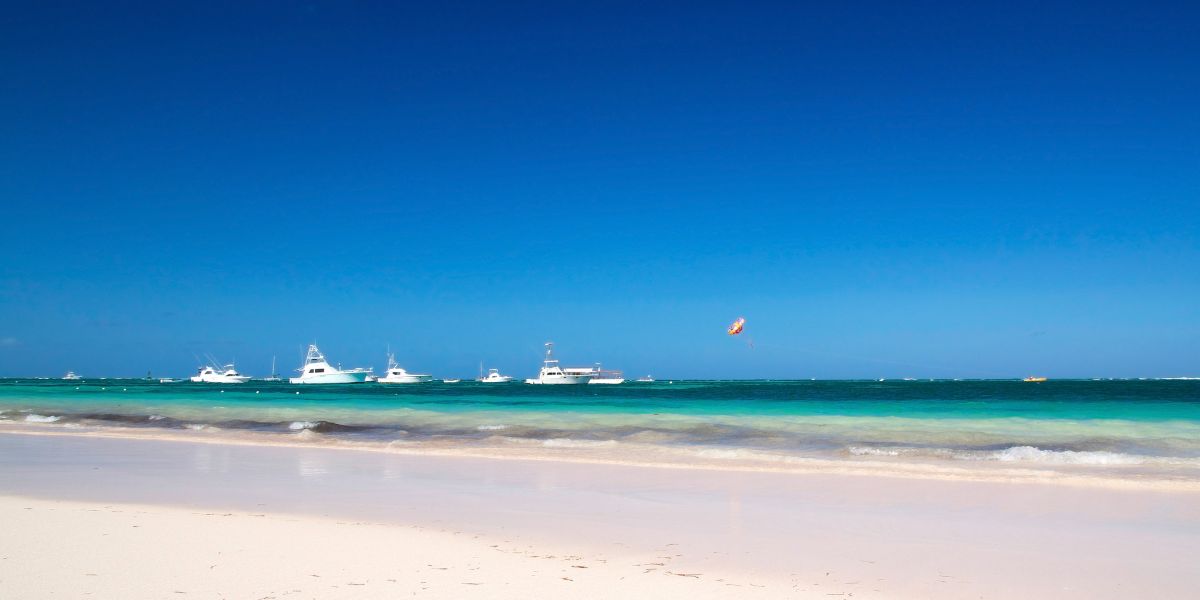 A clear sky and a peaceful Caribbean ocean all in one frame with small to medium boats hanging around near the shore.